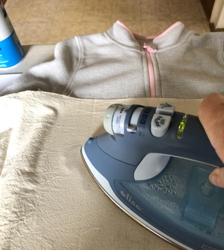 An iron fusing the stitch-outs to the sweater through the pressing cloth.