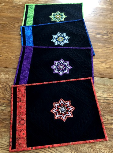 4 black place mats with embroidery and binding in jewel colors.