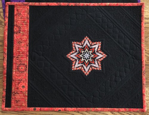 A black place mat with the red embroidery and binding.