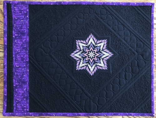 A black place mat with the purple embroidery and binding