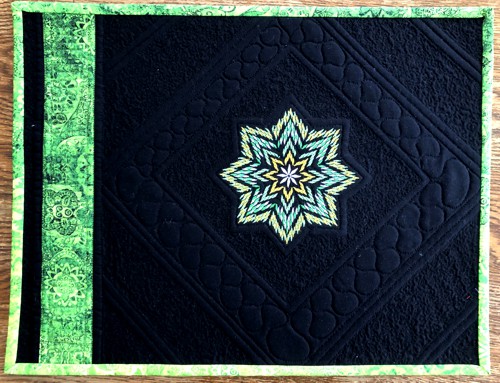 A black place mat with the green embroidery and binding