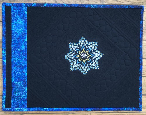 A black place mat with the blue embroidery and binding