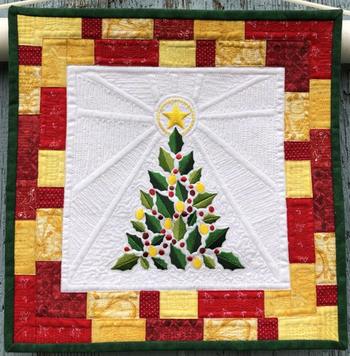 A small Christmas-themed quilt made of white, golden, red and green scraps with embroidery of a Chritmas tree in the center.