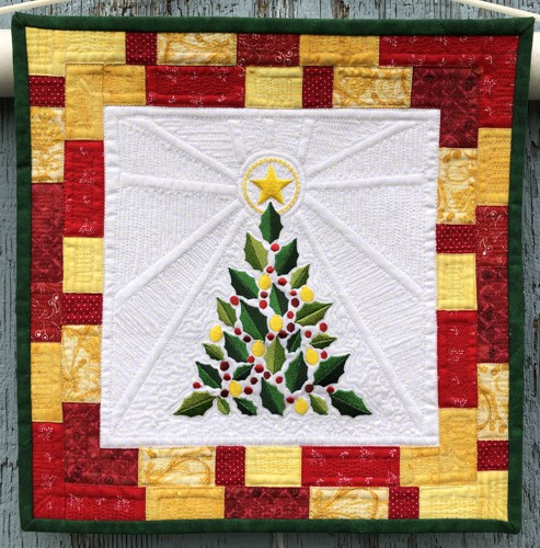A small Christmas-themed quilt made of white, golden, red and green scraps with embroidery of a Chritmas tree in the center.