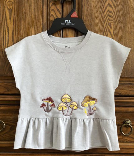 A T-shirt for a child with mushroom applique on the front.