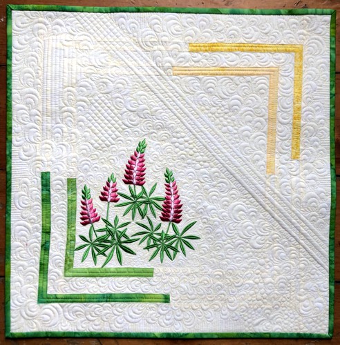 Small pale cream quilt with embroidery of lupine flowers in bright pink and green colors