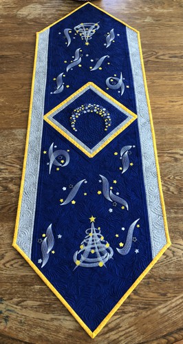 Royal blue quilted tablerunner with embroidery of a moon, stars and Christmas trees in silver and golden colors