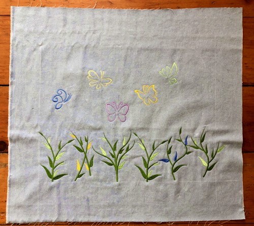 Embroidery of grass ans butterflies on a denim panel.