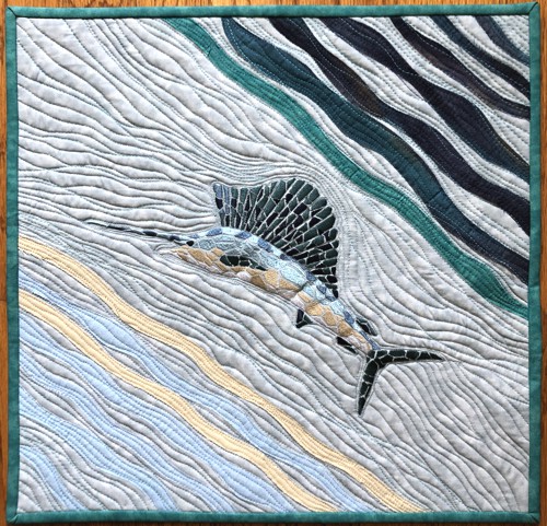 Small quilt in blue and grey hues with embroidery of a swordfish.