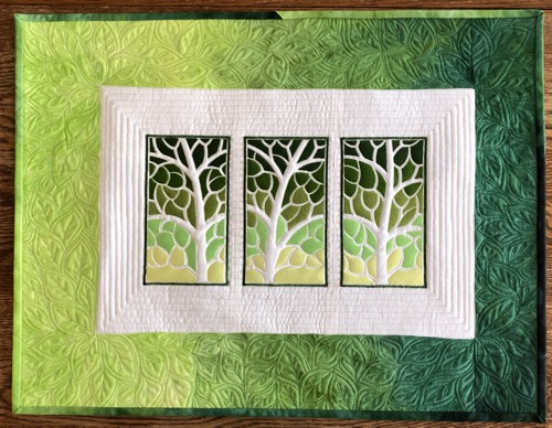 Small quilt in green hues with embroidery of 3 tree panels.