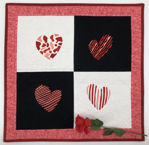 A small quilt with alterating white and black blocks and red hearts embroidery