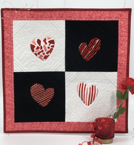 A small quilt with alterating white and black blocks and red hearts embroidery