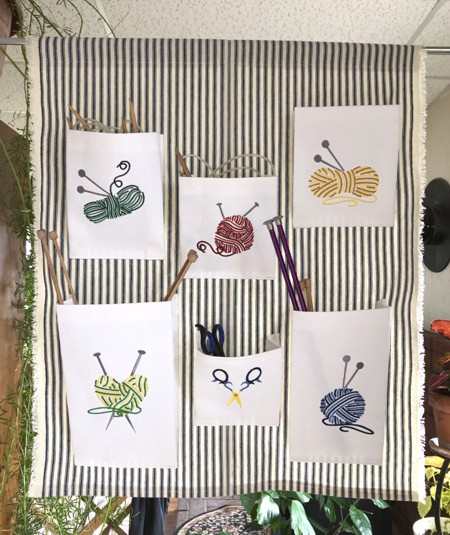 Canvas wall organizer with balls of yarn and scissors embroidery on its 6 pockets