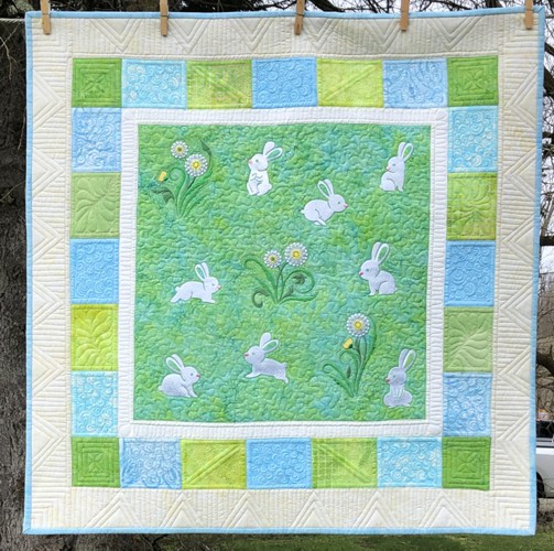 A small wall quilt for a nursery with embroidery of bunnies and dandelions in the central part, with 3 borders , all in green and blue shades.