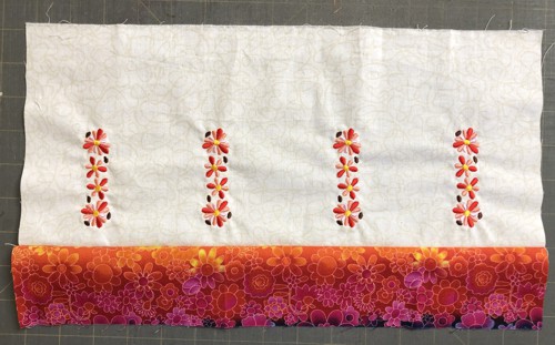 the colored strip is stitched to the lower edge of the embroidered panel.