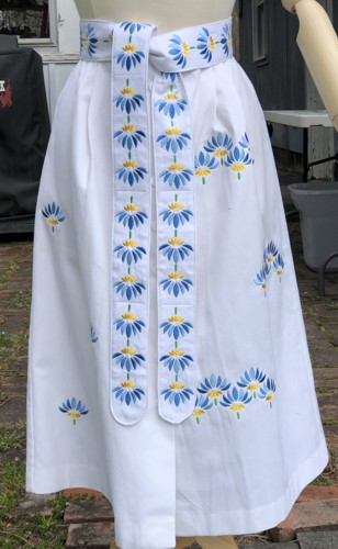 White summer skirt decorated with floral embroidery in blue colors and embroidered sash