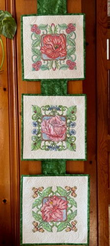 Three quited squares with embroidery of flowers assembled on a piece of ribbon.