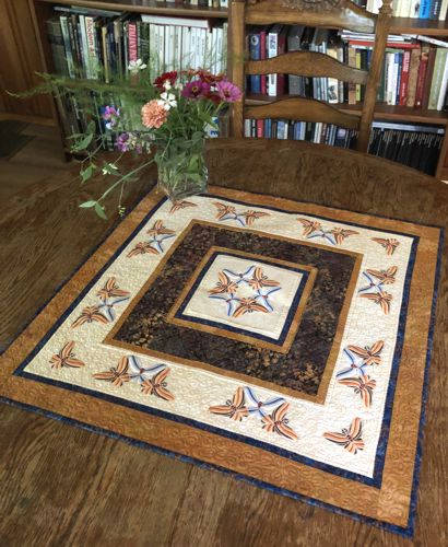 A quilted tabletopper in golden, beige and brown hues with butterfly embroidery.