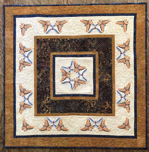 A quilted tabletopper in golden, beige and brown hues with butterfly embroidery.