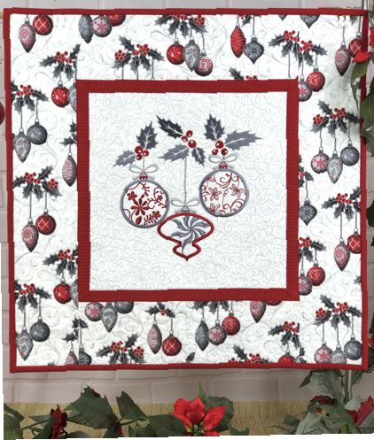 A small wall quilt in red-and-gray colors with embroidery of Christmas ornaments in the center.