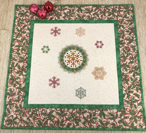 Quilted tabletopper with snowflake embroidery in the center and borders in Christmas patterned fabric.