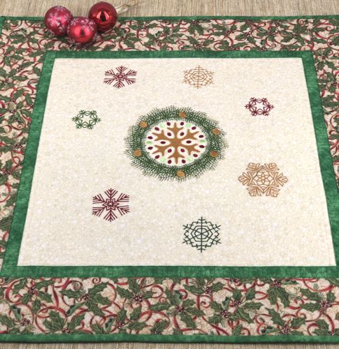 Quilted tabletopper with snowflake embroidery in the center and borders in Christmas patterned fabric.