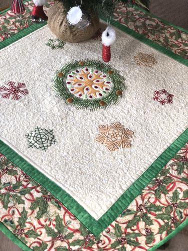 Quilted tabletopper with snowflake embroidery in the center and borders in Christmas patterned fabric.