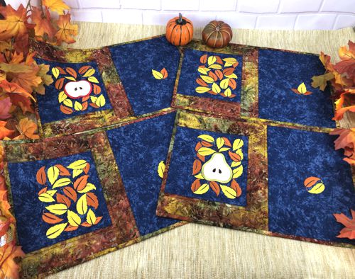 Four quilted placemats with autumn-themed embroidery on the blue background.