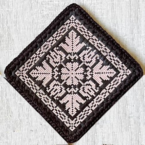 An embroidered square with crocheted edges.