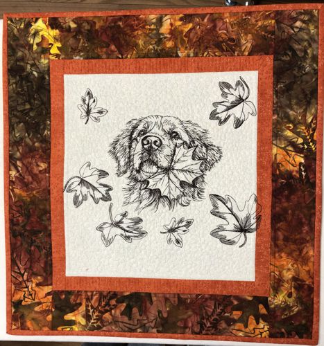 FInished quilt with one-color embroidery of a golden retriever and leaves in the center.