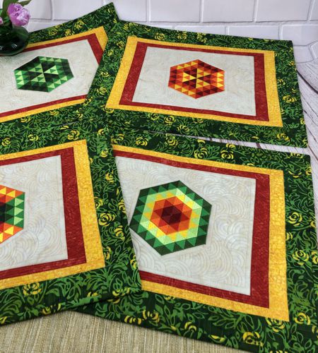 2 quilted placemats with hexagon embroidery on the cream background and red, yellow and green borders.