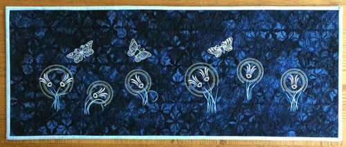 Dark blue wall quilt with embroidery of flowers and butterflies in moonlight hues.