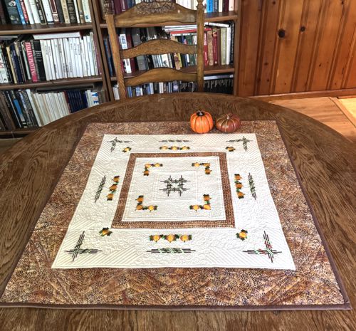 Quilted tabletopper in cream and brown hues with embroidery of pumpkins.
