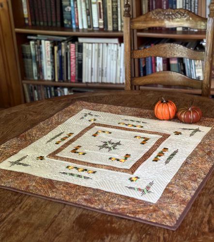 Quilted tabletopper in cream and brown hues with embroidery of pumpkins.