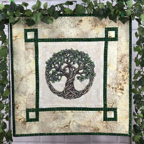 A small light-colored quilt with embroidered Celtic Tree of Life in the center