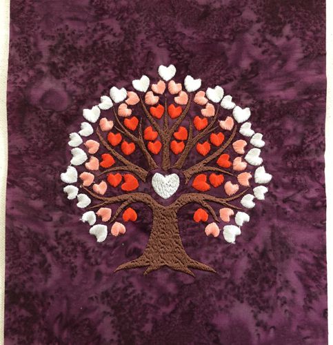 A stitch-out of a tree with hearts as blossoms on a burgundy background.