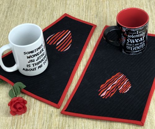 2 finished mug rugs with heart embroidery on a table.