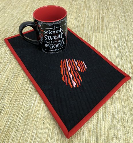 A finished mug rug with heart embroidery on a table.
