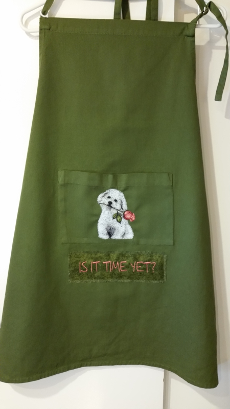 An green apron with the embroidery of a dog on the pocket.